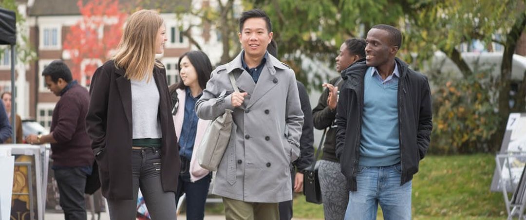 Three students talking and walking with more students in the background